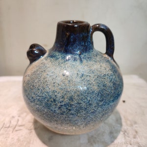 May include: A small, round ceramic jug with a blue and white glaze. The jug has a brown rim and a handle.