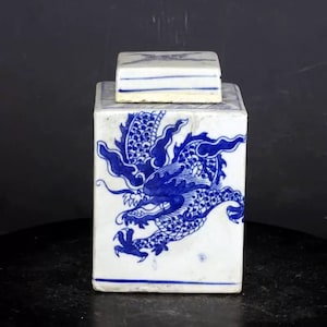 Op de afbeelding: Een vierkante porseleinen pot met een deksel, versierd met een blauw en wit drakenmotief. De pot is in traditionele Chinese stijl.