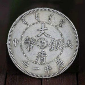 以下が含まれることがあります： 「大清銀幣」 (ダイチンギンヘイ) と「壹圓」 (イチエン) の文字が刻まれた銀製の中国の硬貨。硬貨は小さな文字の円に囲まれています。