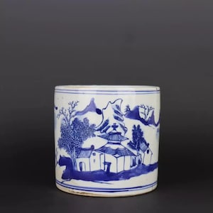 May include: A white ceramic cylinder with a blue and white landscape design. The design features a pagoda, trees, and mountains. The cylinder is approximately 10 inches tall.