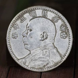 以下が含まれることがあります： 口ひげを生やした男性の横顔と漢字が描かれた銀貨。コインには詳細な縁と花の模様があります。コインの表面には摩耗の兆候が見られ、古くなっていることを示しています。