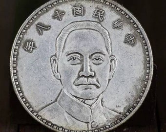 Könnte beinhalten: Silbermünze mit einem Porträt eines Mannes mit Schnurrbart und den chinesischen Schriftzeichen "民國" und "壹圓" auf der Vorderseite.