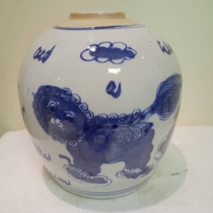Puede incluir: Un tarro de cerámica blanca con diseños pintados en azul y blanco. El tarro presenta un diseño de león azul y blanco con una nube encima. El tarro tiene una forma redonda y una boca ancha.