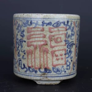 Peut inclure: Une tasse en céramique blanche avec des motifs peints bleus et roses. La tasse a un glaçage craquelé et présente un grand caractère chinois en rose.