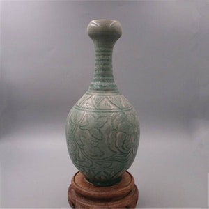 Könnte beinhalten: Eine grün glasierte Keramikvase mit langem Hals und einem bauchigen Körper. Die Vase ist mit einem geschnitzten Blumendesign verziert.