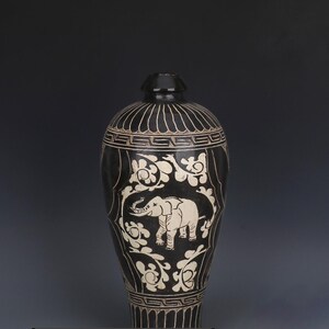 May include: A black ceramic vase with a white elephant design. The vase has a rounded body and a narrow neck. The elephant is surrounded by floral patterns. The vase is approximately 12 inches tall.