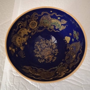 Puede incluir: Un cuenco de cerámica azul con un borde dorado y diseños intrincados de oro de dragones y motivos florales.