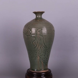 May include: A tall, green glazed ceramic vase with a bird design. The vase has a narrow neck and a wide, rounded body. The bird is in relief and has a detailed design.