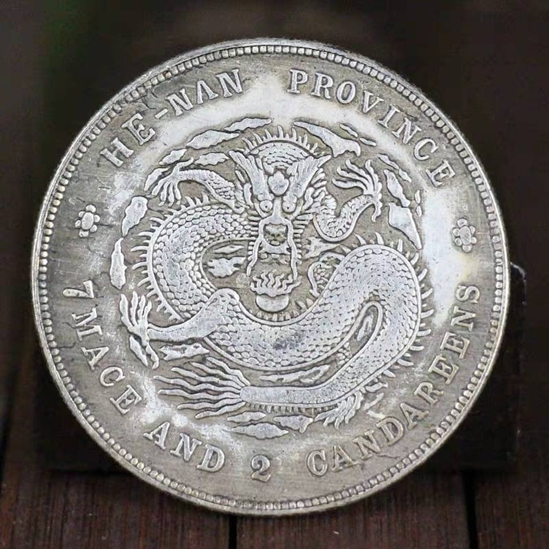 Pode incluir: Uma moeda chinesa de prata com um desenho de drag&atilde;o e a inscri&ccedil;&atilde;o "HE-NAN PROVINCE 7 MACE AND 2 CANDAREENS".