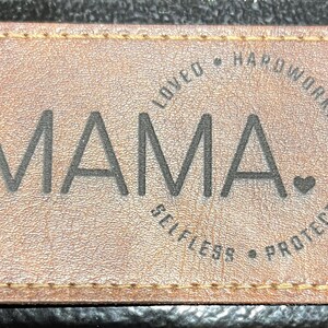 May include: Brown leather patch with stitched edges and the word "MAMA" in black lettering. The text "Loved, Hardworking, Selfless, Protective" is written in a circle around the word "MAMA".