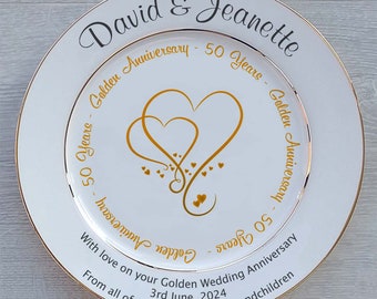 May include: White ceramic plate with a gold rim and a gold design of two intertwined hearts. The text "David & Jeanette Golden Anniversary - 50 Years - Golden Anniversary - 50 Years" is written in gold around the hearts. The text "With love on your Golden Wedding Anniversary 3rd June, 2024 From all of your children and grandchildren" is written in black at the bottom of the plate.