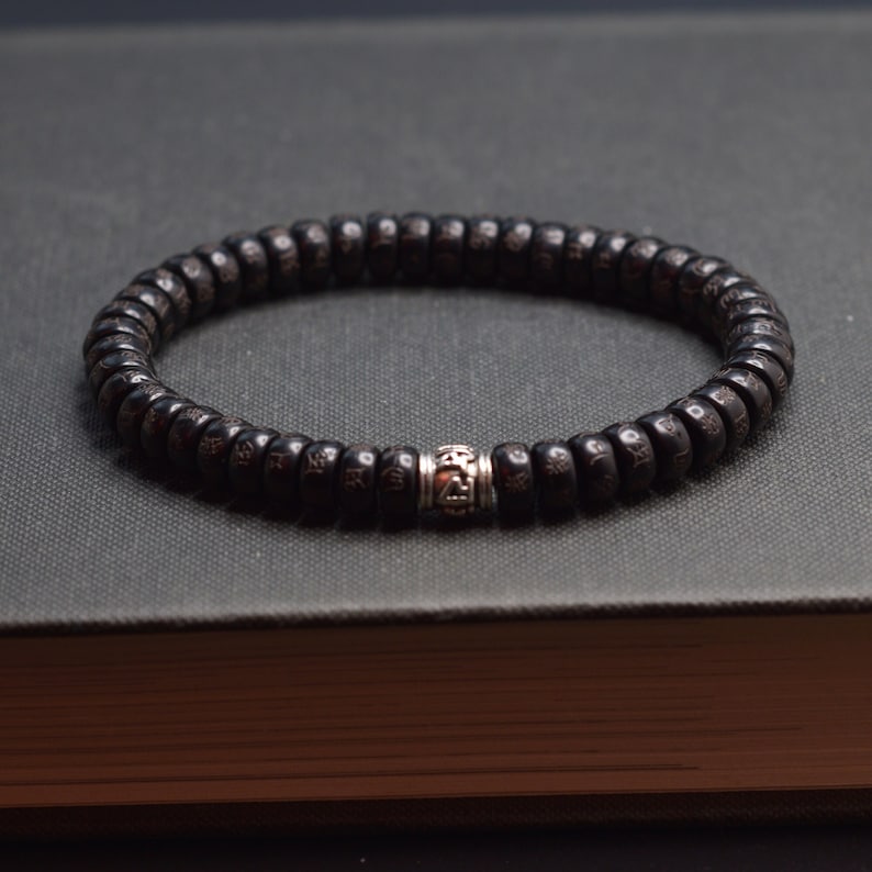 May include: A black wooden beaded bracelet with a silver bead in the center. The beads are small and round, and the bracelet is simple in design.