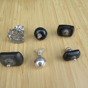 Può includere: Una collezione di sei pomelli con forme e finiture varie. Sono inclusi un pomello argentato a forma di fiore, due pomelli sferici neri lisci, due pomelli neri rettangolari con bordi arrotondati e un pomello a sfera in argento lucido.
