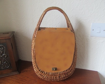 May include: A brown wicker handbag with a tan leather flap and a metal clasp. The bag has a single handle.