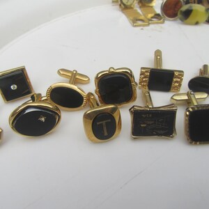 May include: A collection of gold-toned cufflinks with black onyx or onyx-like insets. Some cufflinks have a single diamond or crystal accent. Various shapes include square, oval, and octagonal. Some cufflinks have a letter "T" on them.