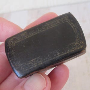 May include: A small black leather box with gold trim. The box is rectangular in shape and decorated with a geometric pattern.