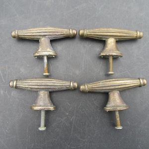 Op de afbeelding: Vier antieke messing kastknoppen met een geribbeld, tonvormig ontwerp. Elke knop heeft een decoratieve basis en een schroefdraad voor montage. De knoppen zijn gerangschikt op een donkergrijze ondergrond.