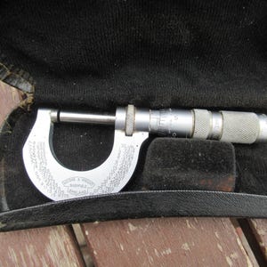 May include: A silver metal micrometer with a C-shaped frame featuring engraved decimal equivalents and the text Moore & Wright Sheffield England. The tool has a knurled adjustment knob and a graduated sleeve, presented in a black velvet-lined case.