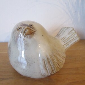 May include: A ceramic bird figurine with a white glaze and brown accents. The bird has a round body and a small tail. The bird's eyes are brown and its beak is open.