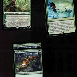 May include: Several Magic: The Gathering trading cards are displayed. The cards feature green and black color schemes with fantasy art. The cards include "Vivien, Champion of the Wilds", "Genesis Wave", and "Wildborn Preserver".
