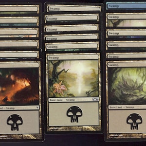 May include: A collection of Magic: The Gathering "Swamp" basic land cards. Each card features swamp-themed artwork, a mana symbol, and the text "Swamp". The cards are in various conditions.