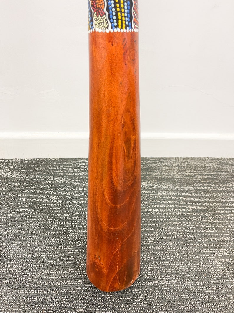May include: A wooden didgeridoo with a colorful, patterned band around the top. The didgeridoo is brown and has a natural wood grain.