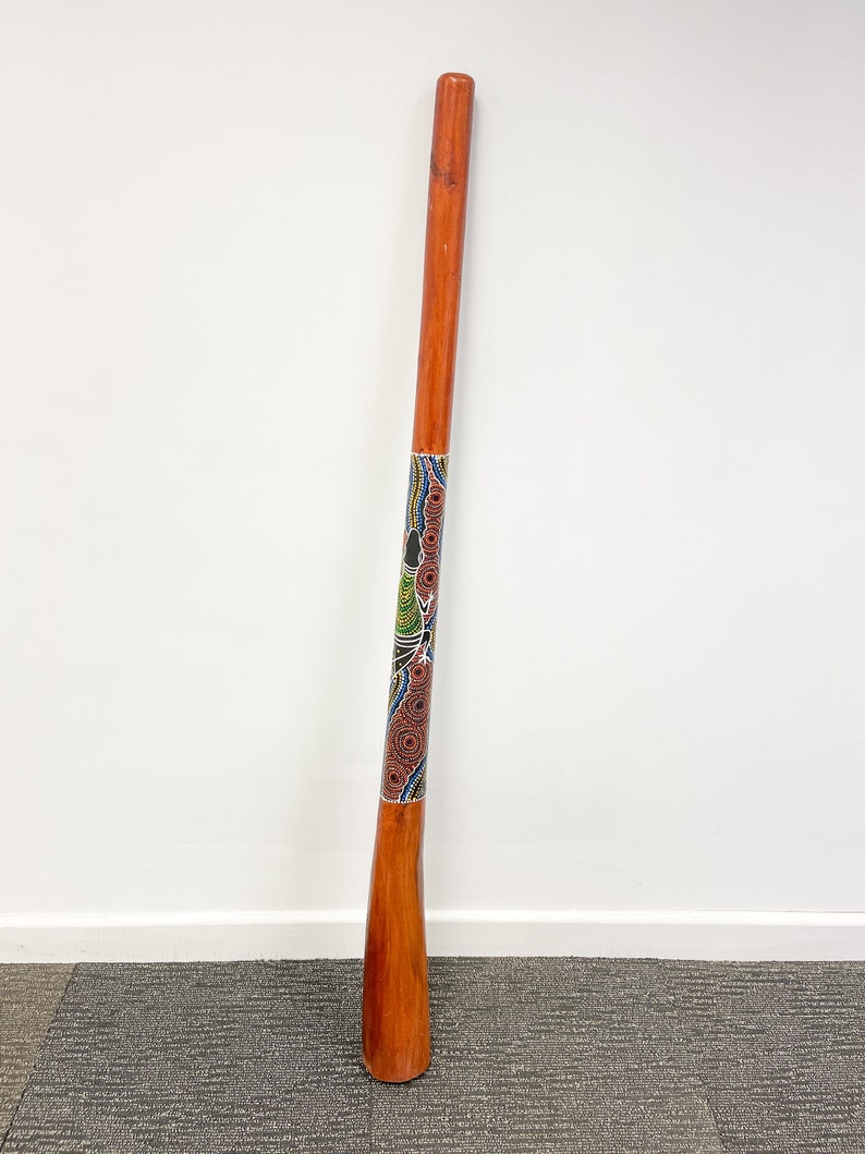 May include: A wooden didgeridoo with a colorful Aboriginal art design. The didgeridoo is brown with a blue, green, red, and black painted design.