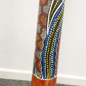 May include: A wooden didgeridoo with a black, white, blue, yellow, and orange painted design. The design features dots and wavy lines.