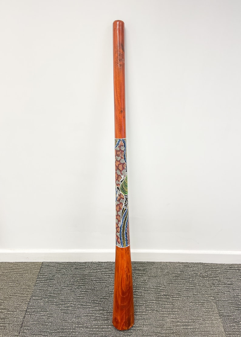 May include: A wooden didgeridoo with a colorful Aboriginal design painted on it. The didgeridoo is brown and has a natural wood finish. The design is a mix of red, blue, green, and yellow.