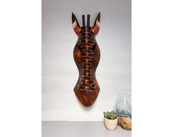 May include: A wooden giraffe head wall decor with a brown and black patterned design. The giraffe head is carved from wood and has a realistic appearance.