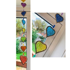May include: A rainbow-colored beaded heart garland with each heart made of glass mosaic tiles. The garland is hanging in a window.