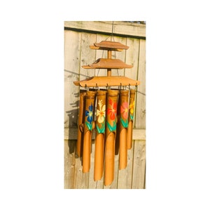May include: A wooden wind chime with a pagoda-style top and eight bamboo tubes painted with colorful flowers. The tubes are suspended from the top by strings and are designed to make a gentle sound when the wind blows.