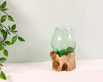 Peut inclure: Un vase en verre vert de forme arrondie est posé sur une base en bois naturel. Le vase est transparent et la base en bois a un aspect rugueux et texturé. Le vase est un objet décoratif. Le vase mesure environ 15 cm de haut.