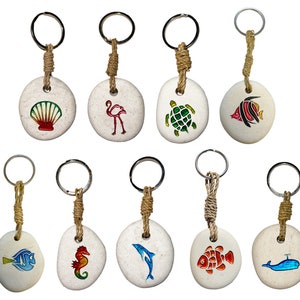 May include: Ten keychains featuring various sea life designs. Each keychain has a white, round stone with a colourful painted design. The designs include a seashell, flamingo, turtle, fish, dolphin, seahorse, and whale. The keychains are made from natural materials and are ideal for adding a touch of coastal charm to your keys.