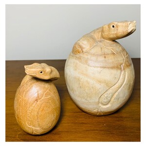 May include: Two wooden sculptures of snakes, one larger than the other. The larger snake is curled around itself, while the smaller snake is coiled in a ball. Both sculptures are made of light brown wood and have a smooth, polished finish.