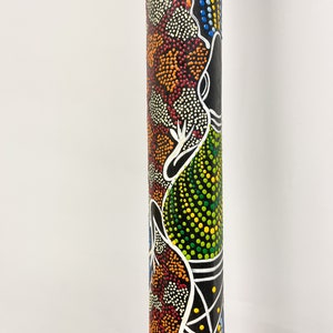 May include: A wooden didgeridoo with a colorful Aboriginal art design. The design features a black, white, green, orange, red, yellow, and blue dot pattern. The didgeridoo is approximately 30 inches long.