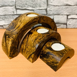 May include: Three wooden candle holders in the shape of arches, each with a different size. The holders are made of dark brown wood with a marbled pattern. The holders are stacked on top of each other, with the largest holder on the bottom and the smallest holder on top.