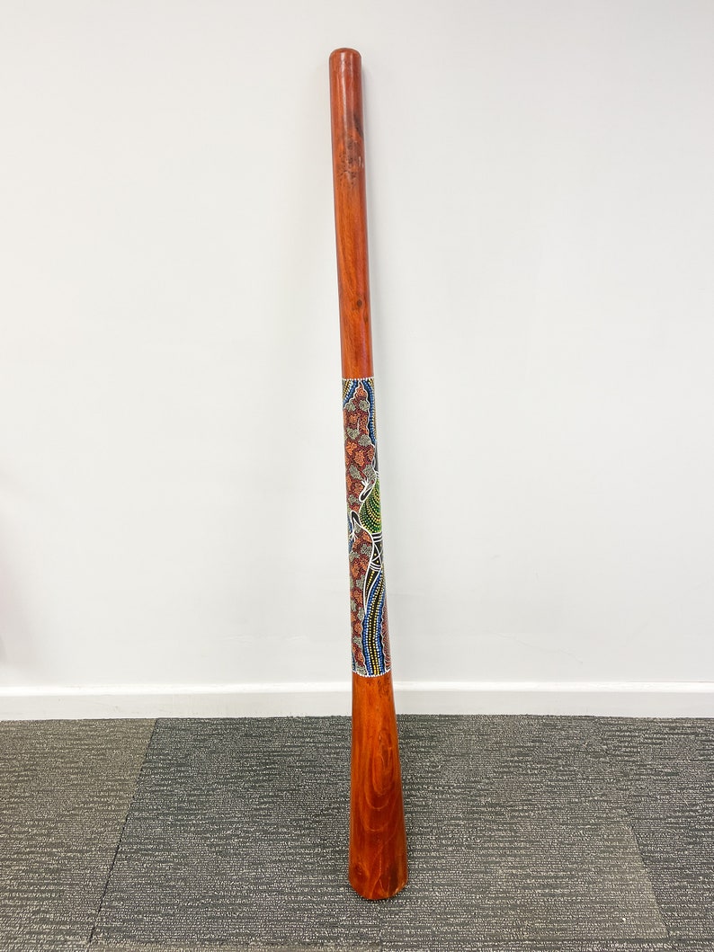 May include: A wooden didgeridoo with a colorful Aboriginal design painted on it. The didgeridoo is about 1.5 meters long and has a natural wood finish.