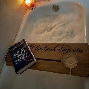 May include: A wooden bath tray with a glass, a book titled "A Court of Mist and Fury" by Sarah J. Maas, and the text "Don't let the hard days win".