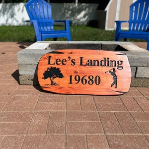 May include: A wooden sign with the text "Lee's Landing 19680" and a silhouette of a golfer. The sign is brown with black lettering and a tree design.