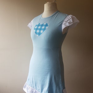 Puede incluir: Un vestido azul claro con un ribete de volantes blancos y un corazón de cuadros azules y blancos en la parte delantera.