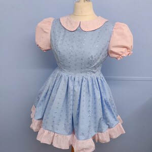 May include: A light blue dress with a pink collar and sleeves. The dress has a white floral pattern and a pink ruffle trim.
