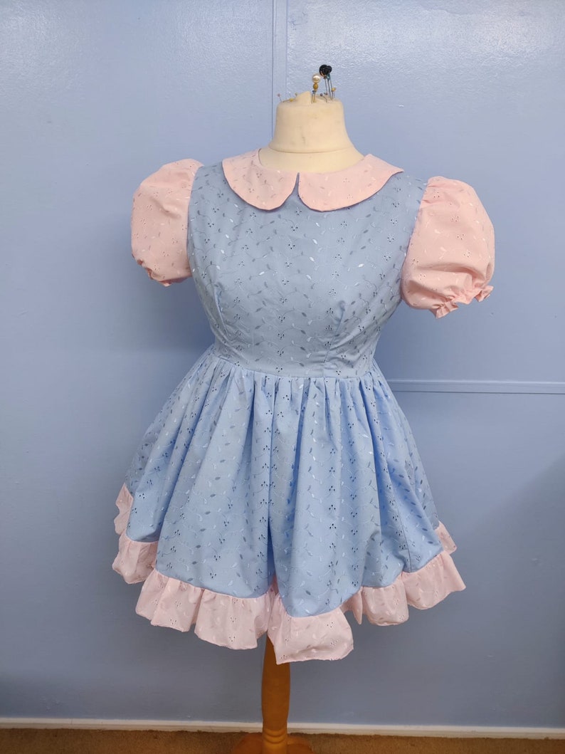 May include: A light blue dress with a pink collar and sleeves. The dress has a white floral pattern and a pink ruffle trim.
