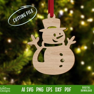 May include: Wooden snowman ornament with a top hat, scarf, and three buttons. The ornament is hanging from a red ribbon. The text "CUTTING FILE" is in a white oval. The bottom of the image has the text "FreeTree Designs" and file type information.