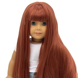 May include: A doll with long, auburn hair and bangs. The doll has blue eyes and is wearing a white t-shirt and denim shorts. The doll's hair is styled in a long, straight fashion, cascading down the front.