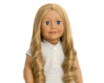 Op de afbeelding: Een pop met lang blond haar, die een lichtgrijze jurk draagt met een gerimpelde zoom en grijze schoenen.