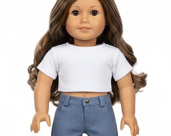 May include: A doll with long brown hair, wearing a white crop top and denim shorts. The doll has brown eyes and is standing against a white background. The shorts have rolled-up cuffs.