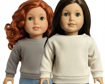 May include: Two dolls with distinct features. The doll on the left has wavy red hair, green eyes, and freckles, wearing a gray long-sleeve sweatshirt and blue jeans. The doll on the right has straight dark brown hair, blue eyes, and wears a cream sweatshirt.
