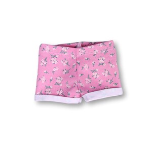 May include: Pink floral print shorts with a white cuff. The shorts have a small floral pattern.