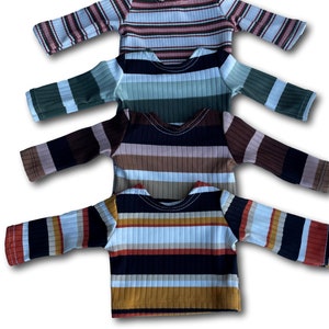 May include: Four striped long-sleeved shirts in different color combinations. The shirts are stacked on top of each other, with the bottom shirt being a black, white, orange, and brown striped shirt.